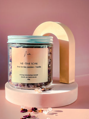 Me-Time Rose de mai soak, photo shows a jar sitting on a raiser with soak salts and petals sprinkled around the jar