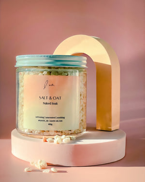 Me-Time Rose de mai soak, photo shows a jar sitting on a raiser with soak salts and colloidal oatmeal sprinkled around the jar